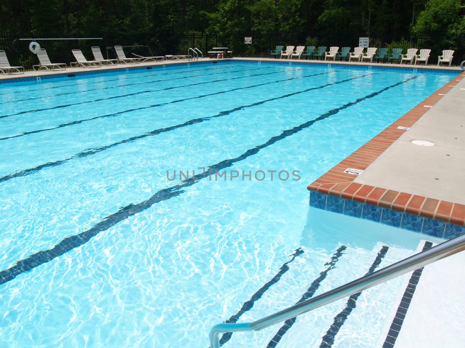 Wide angle image of a large community swimming pool showing the steps, deck, chairs, and lifesaver. 