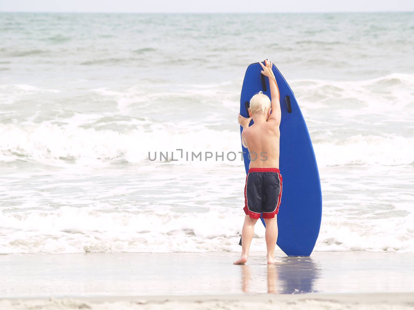 Young boy wrestling with a blue surfboard on a bright day