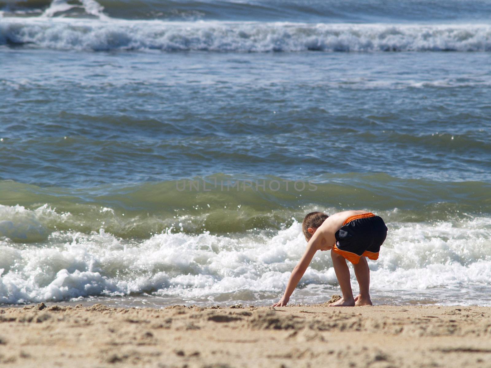 Young boy bending over playing in the sand at the beach. 
