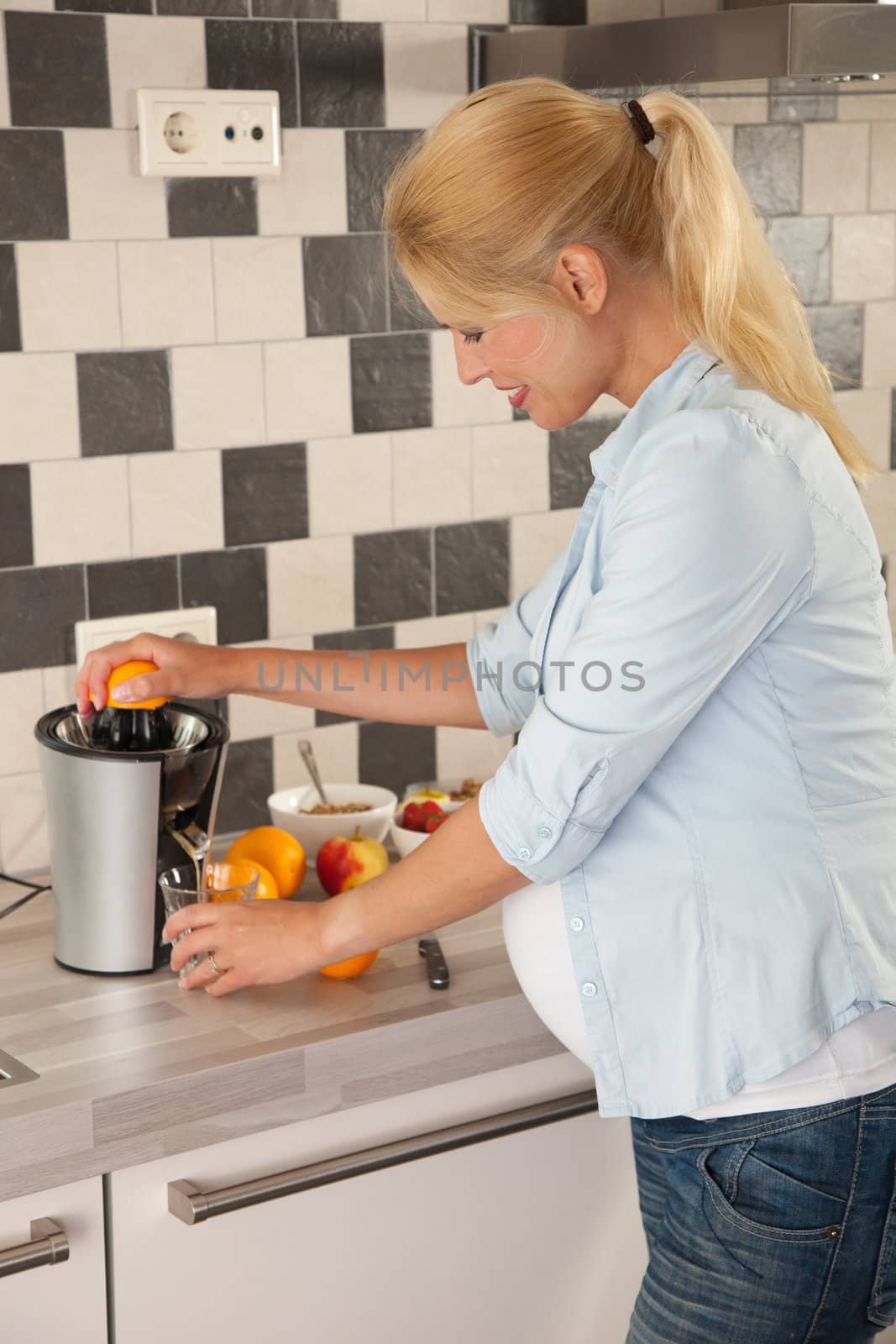 Attractive pregnant woman making orange juice for herself