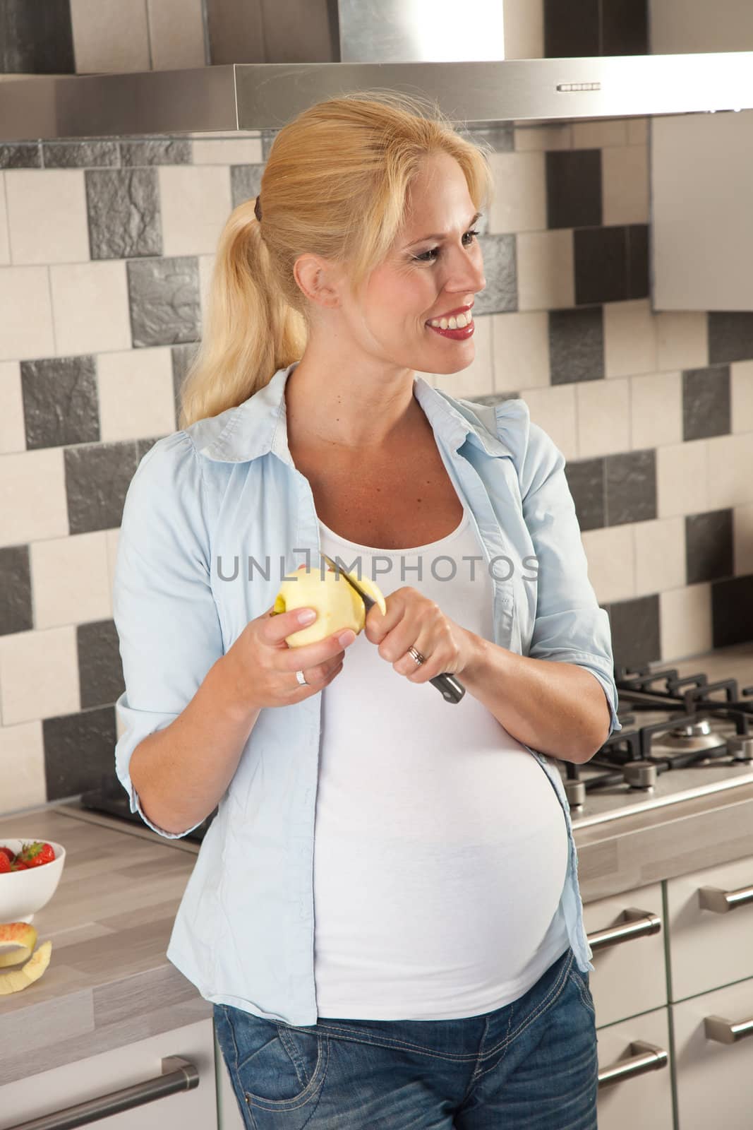 Beautiful pregnant woman standing in the kitchen peeling an apple