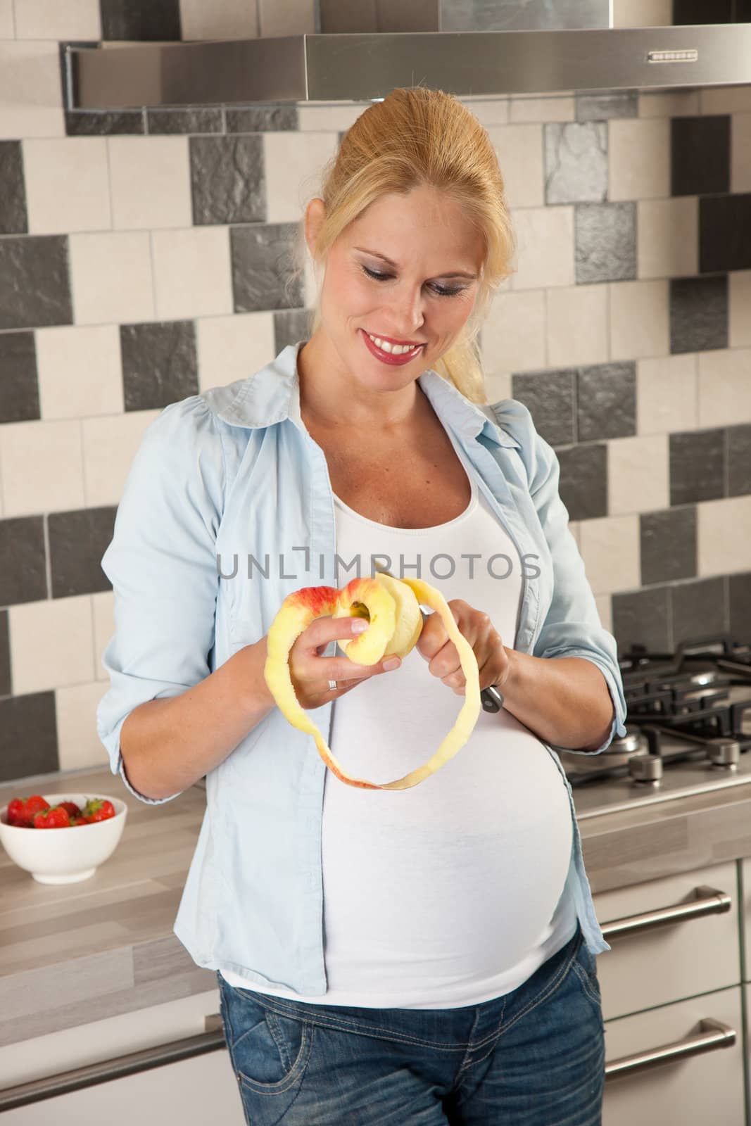 Attractive pregnant woman standing in the kitchen peeling an apple