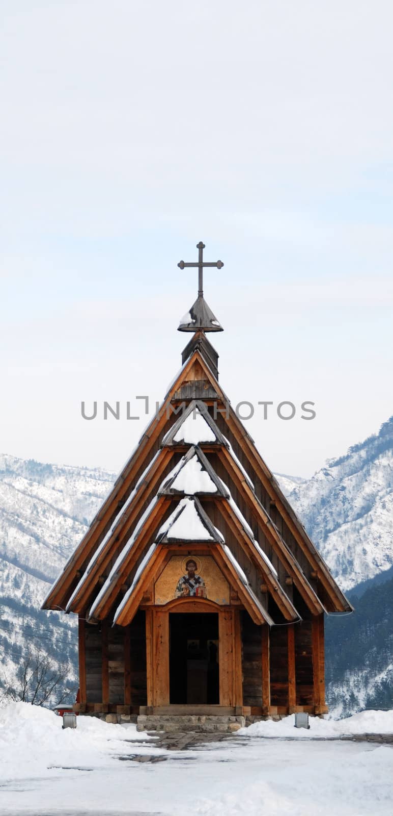 Small wooden Orthodox church on top of a mountain surrounded with snow.
