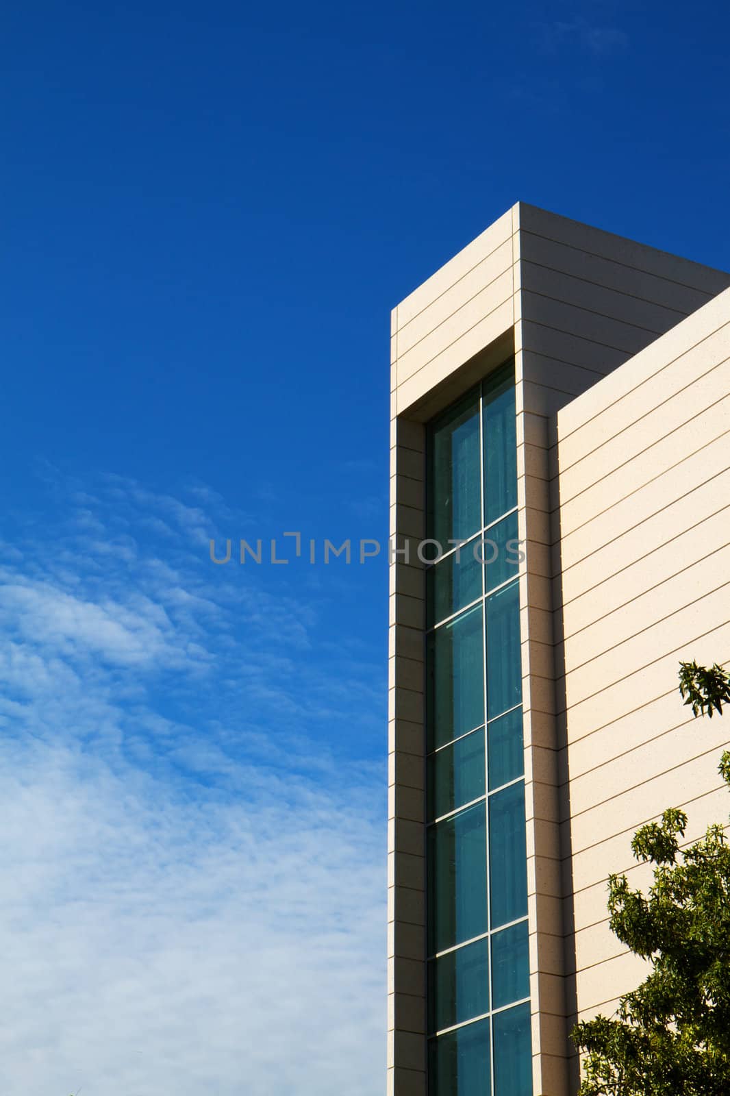 Corner of a building and elevator tower enclosed by green glass with blue sky background