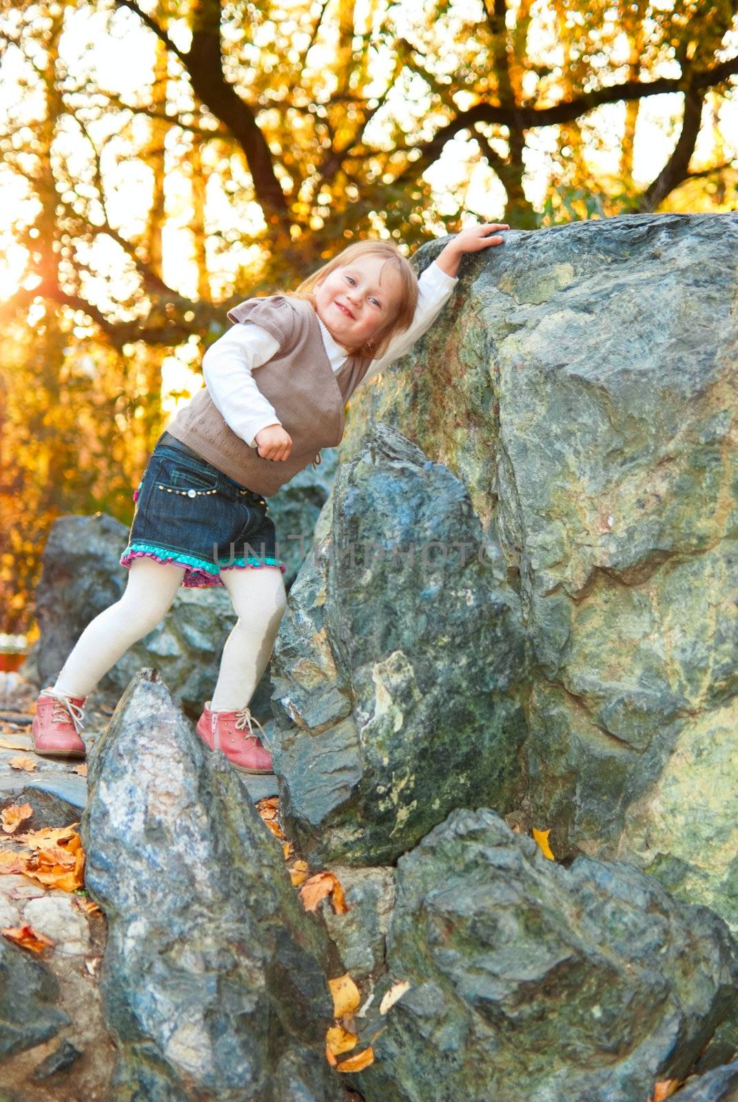 Small girl (3 years old) with smile is touching big rock. Photo has space for text