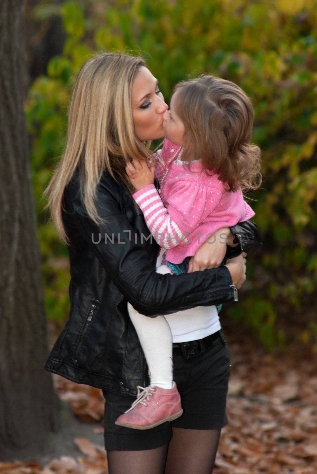 Long haired mother kisses her daughter in autumn park.