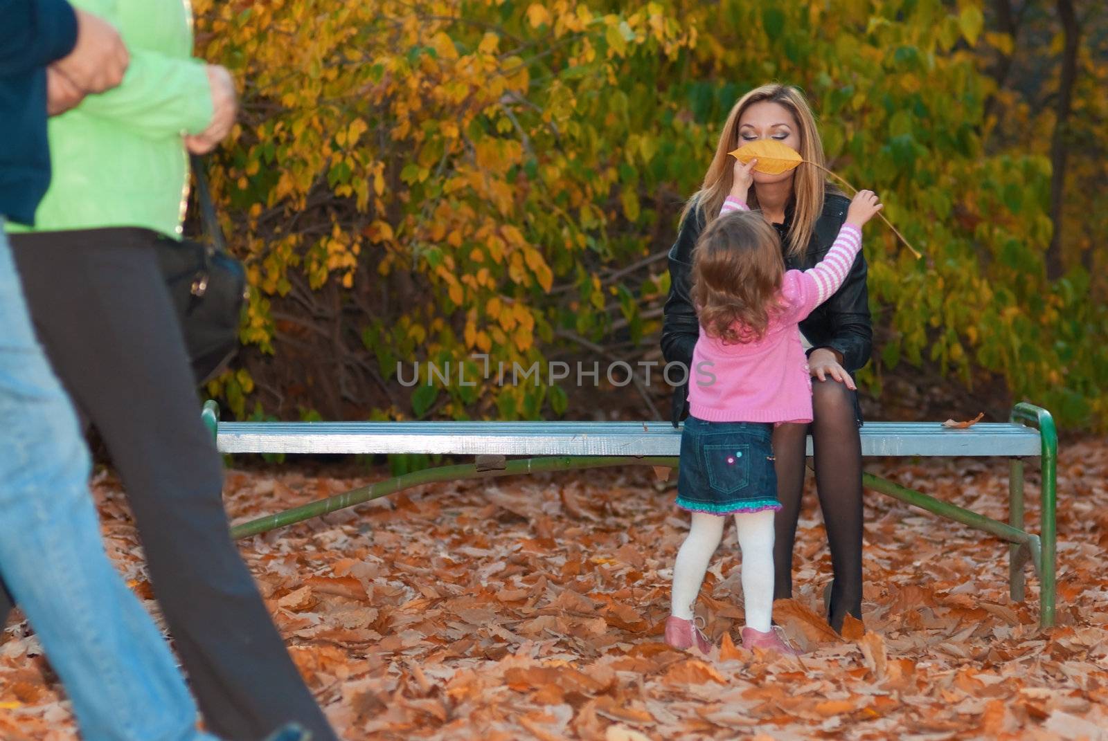 Girl is playing with her mom. She closes moms face with yellow tree leave.