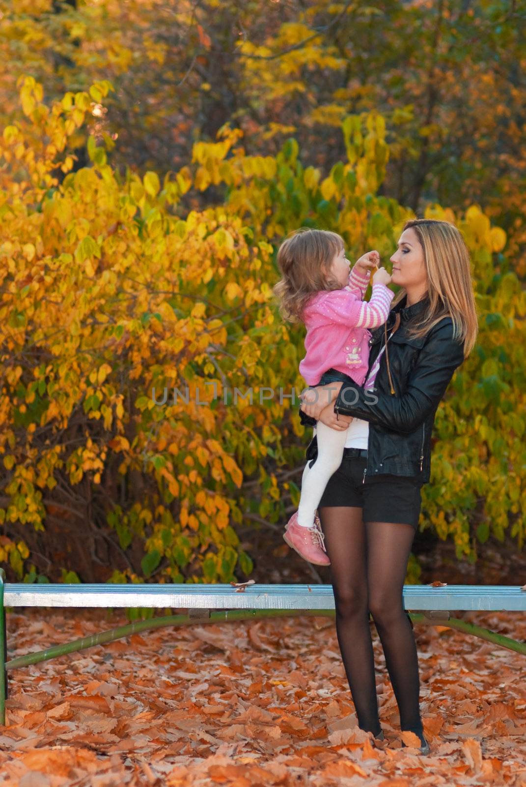 Mother hold her daughter in arms. Girl shows autumn leaf to her mother