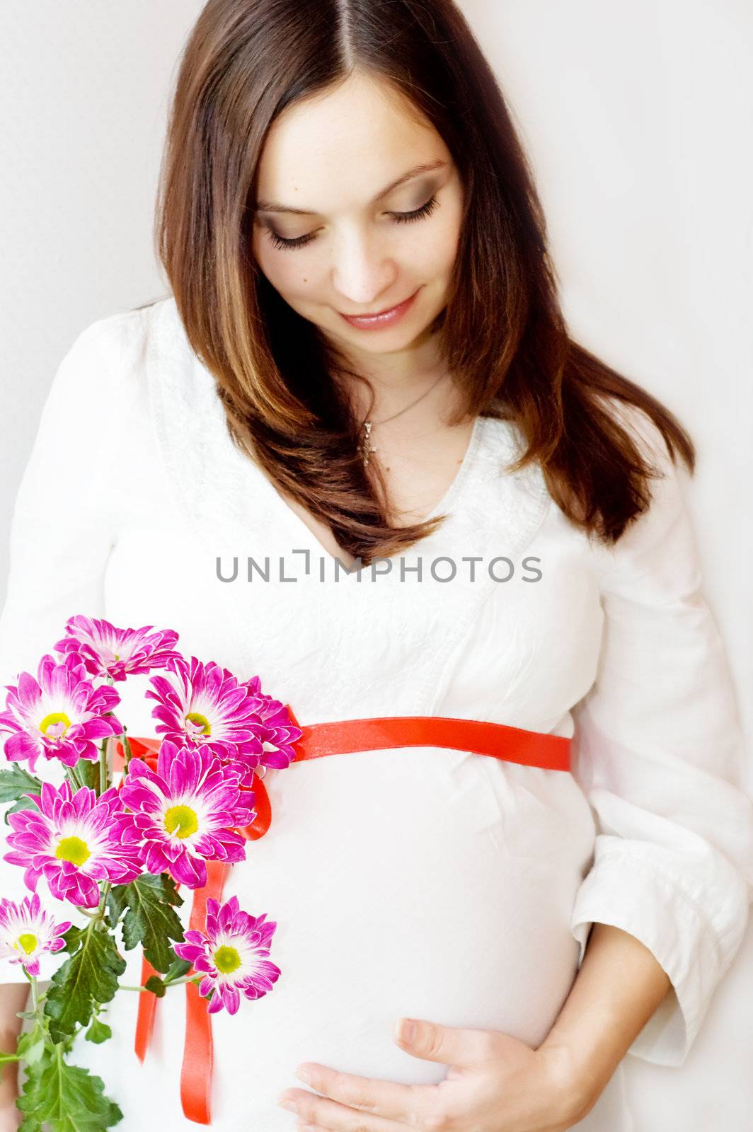 Beautiful pregnant woman holding belly with flowers