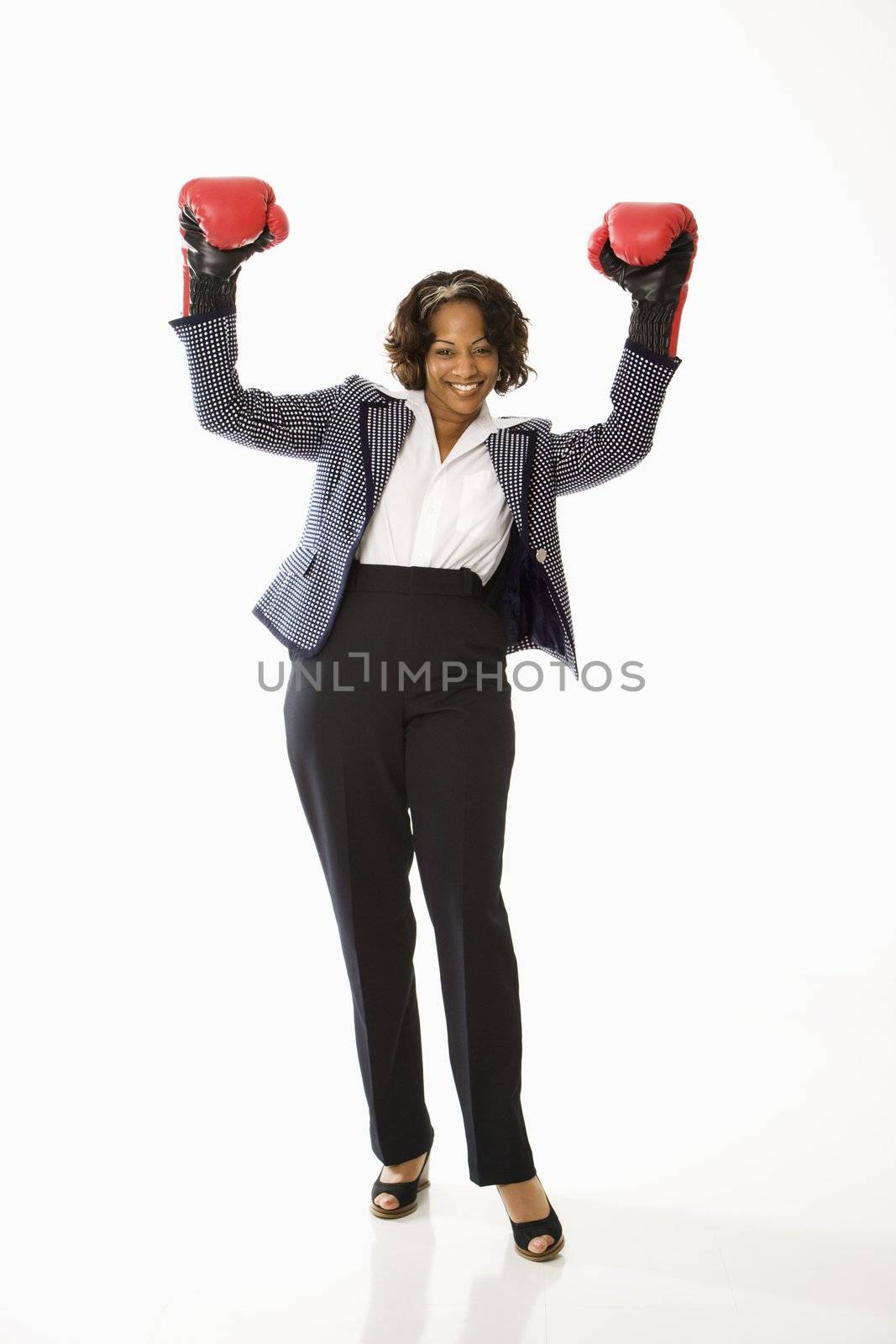 Businesswoman wearing boxing gloves holding arms up in victory stance and smiling.