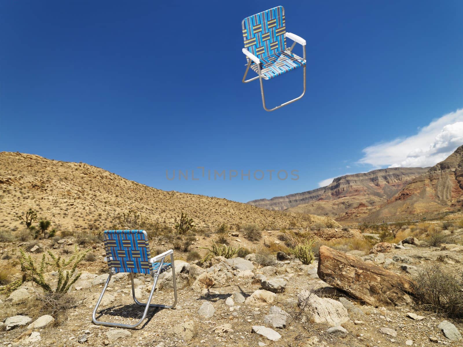 One lawn chair on ground and other up in the air in desert landscape.