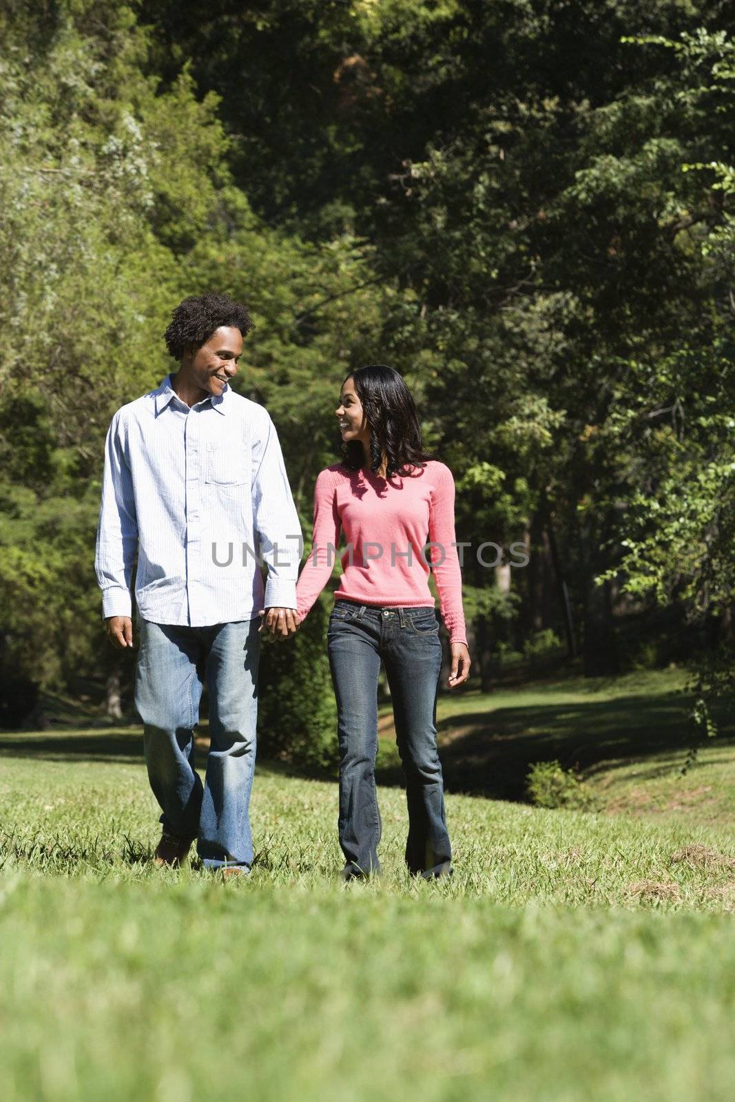 Smiling couple holding hands walking and talking in park.