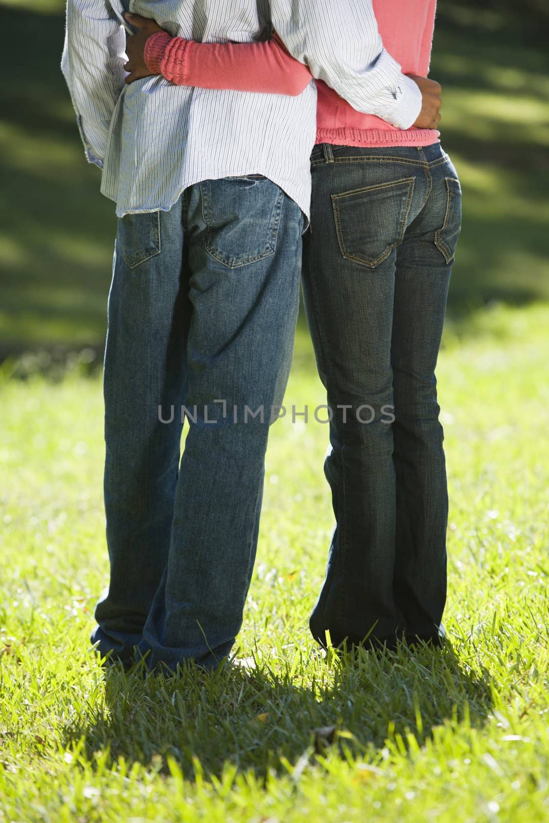 Low view of couple standing in park with arms around eachother.