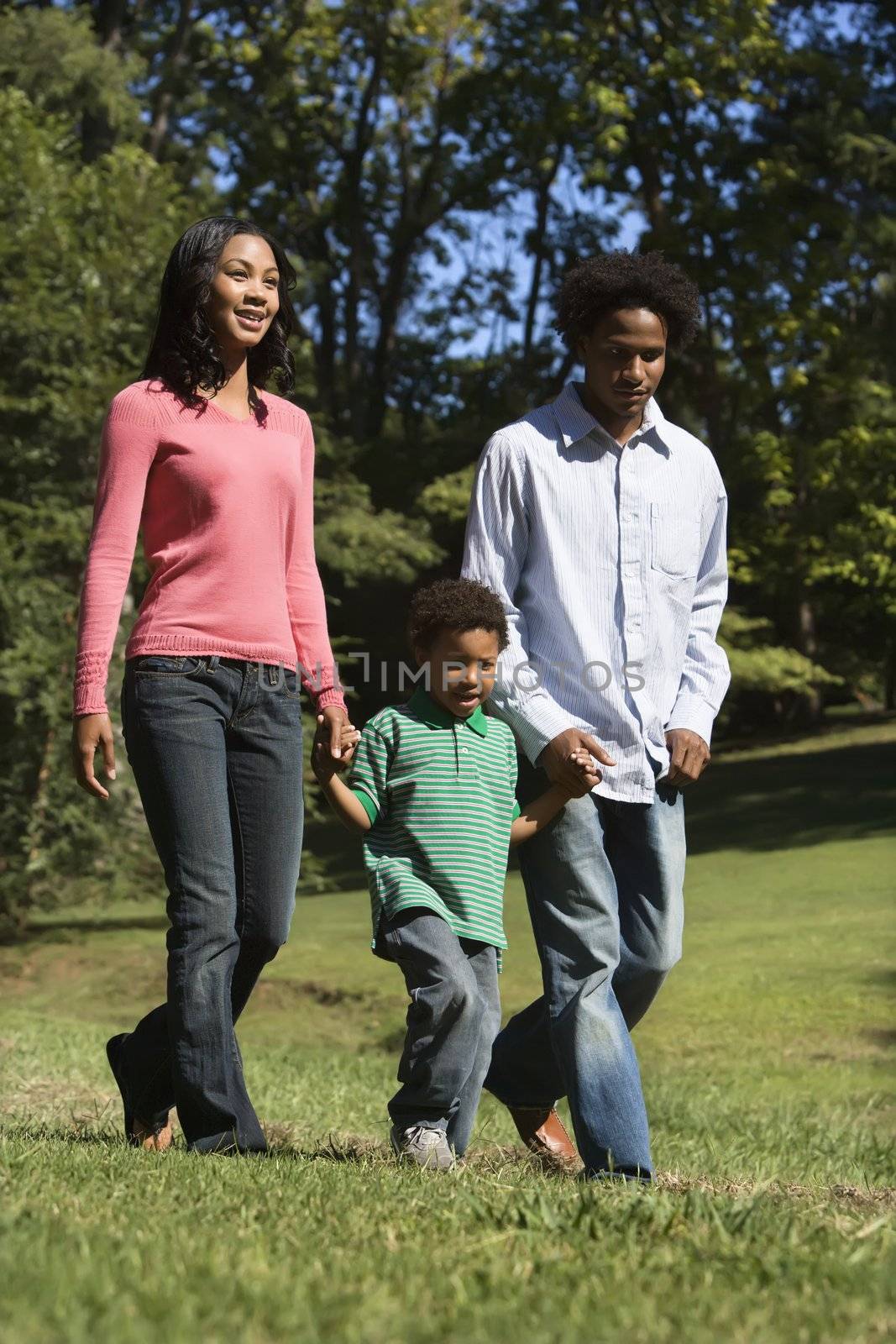 Parents and young son walking in park holding hands.