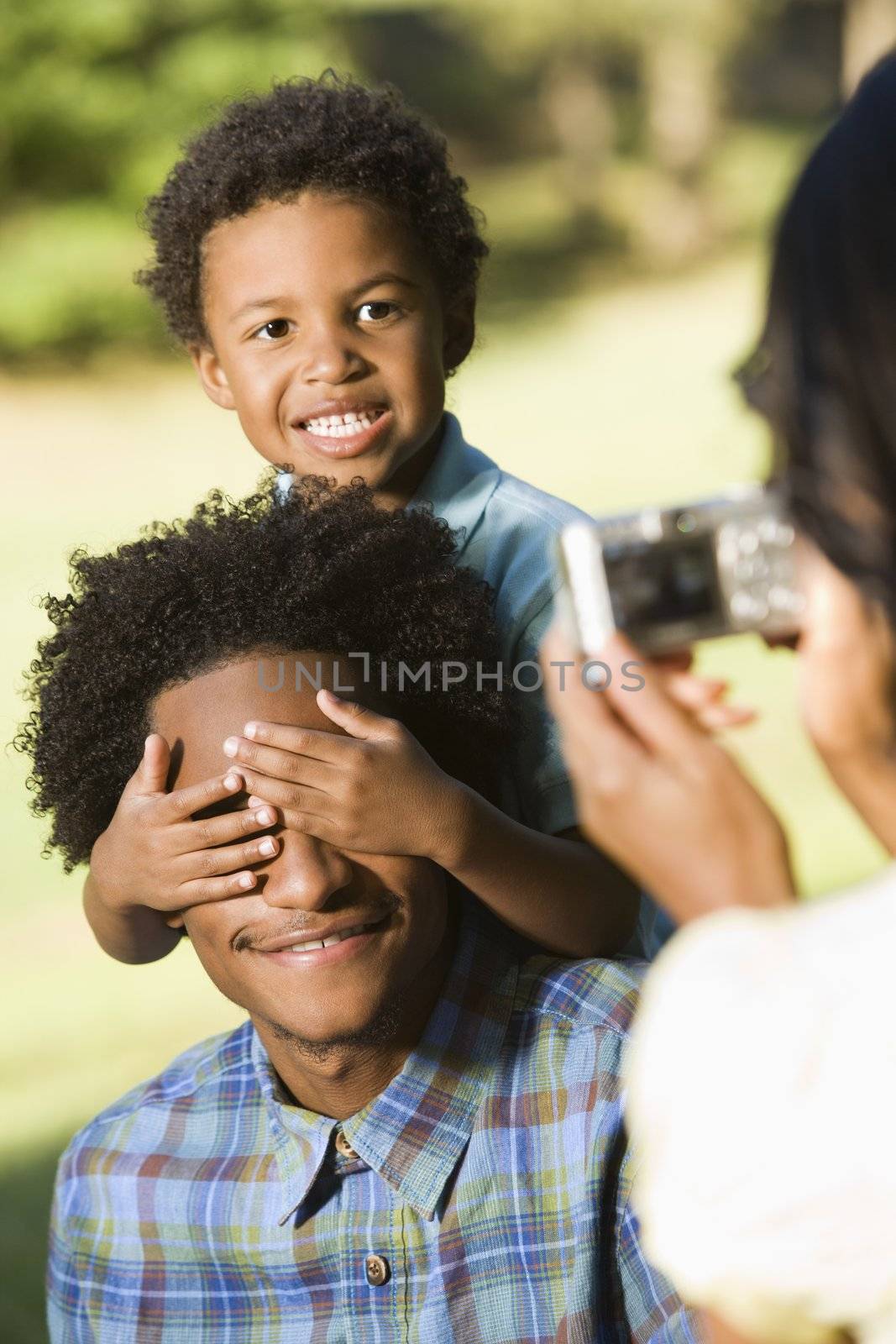Woman taking digital photo of husband and son in park.
