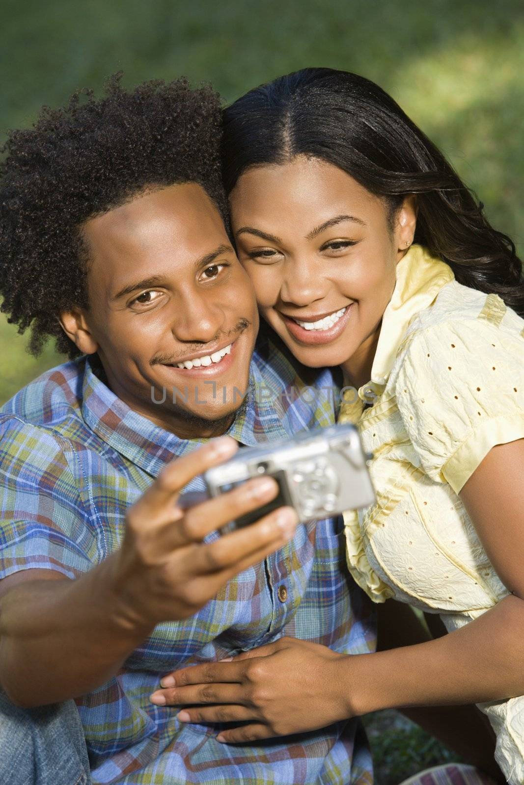 Happy smiling couple taking pictures together in park with digital camera.