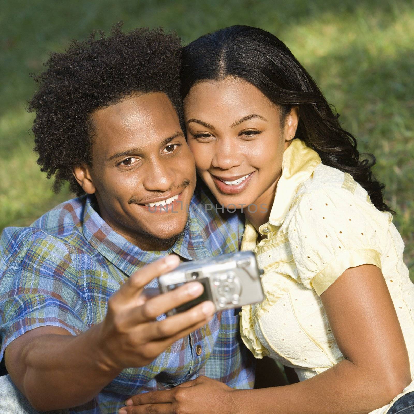 Happy smiling couple taking pictures together in park with digital camera.