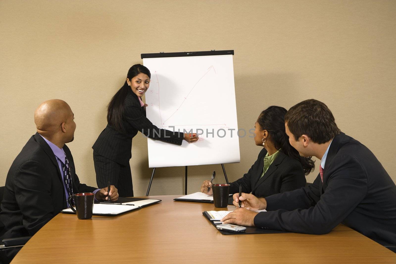 Businesspeople sitting at conference table smiling while businesswoman gives presentation.