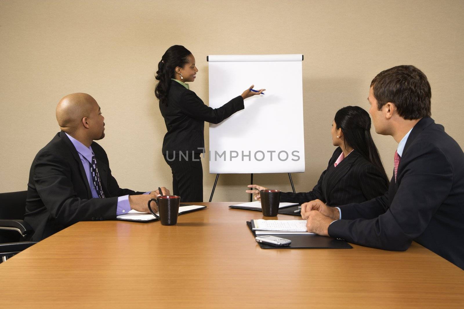 Businesspeople sitting at conference table while businesswoman gives presentation.