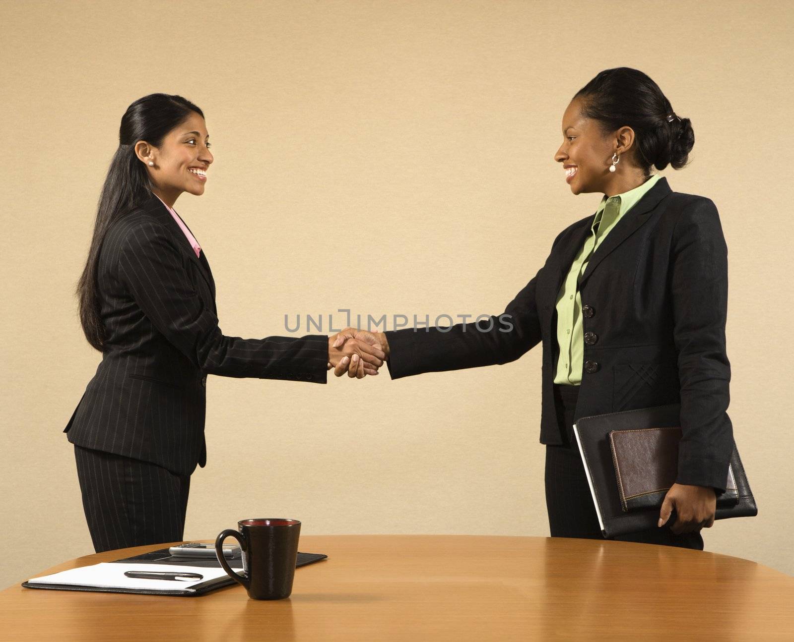 Two businesswomen in suits shaking hands and smiling.