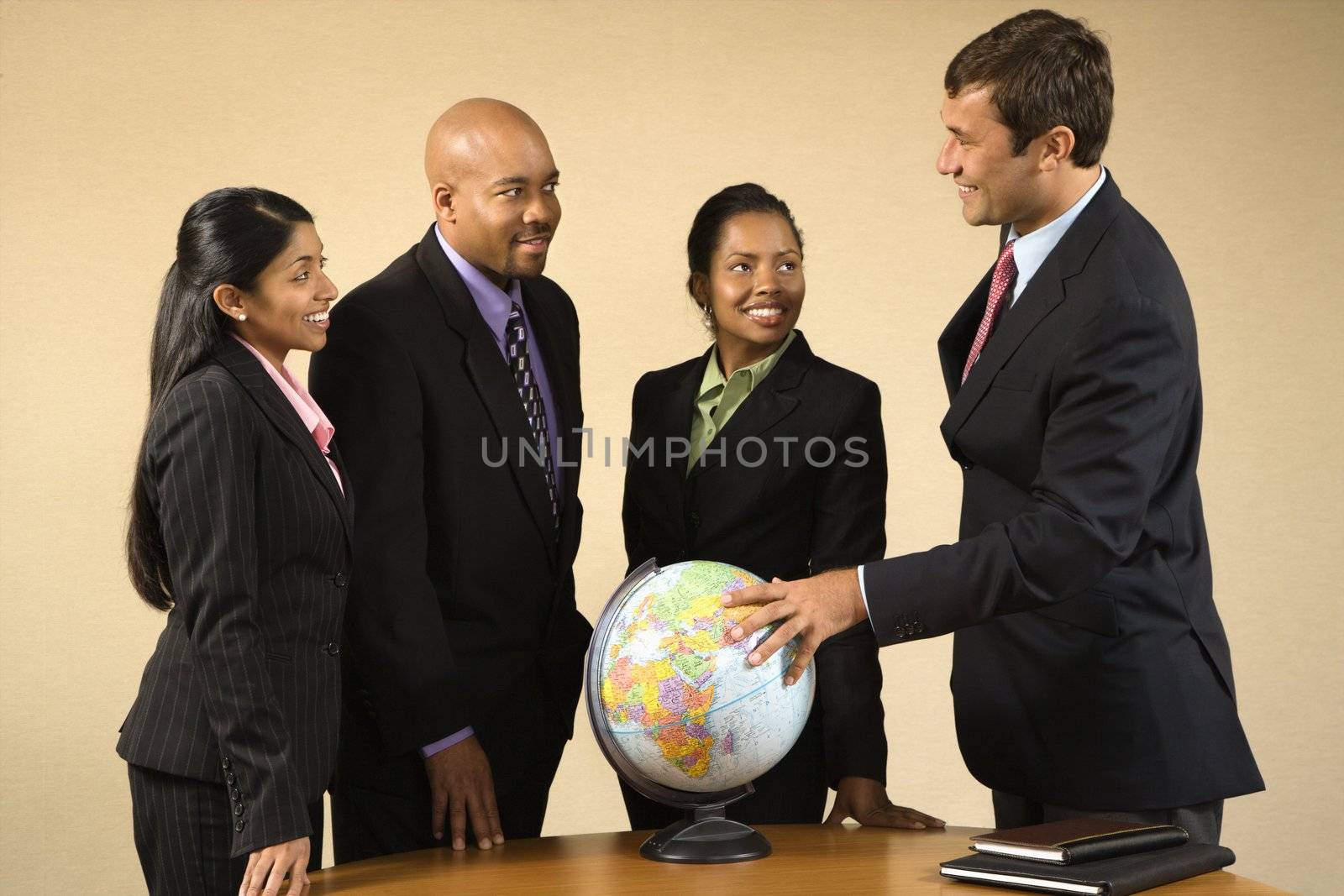 Corporate businesspeople standing around world globe smiling and talking.