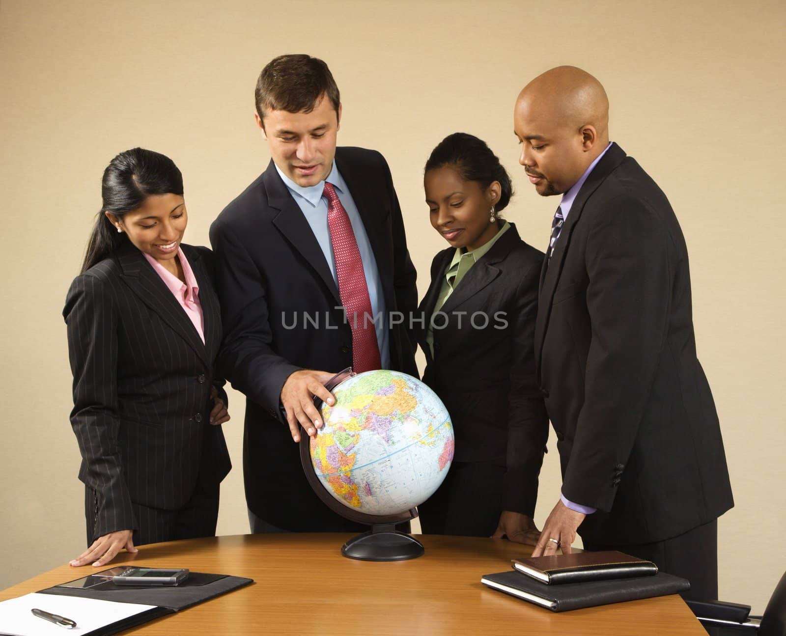 Corporate businesspeople standing around world globe smiling and talking.