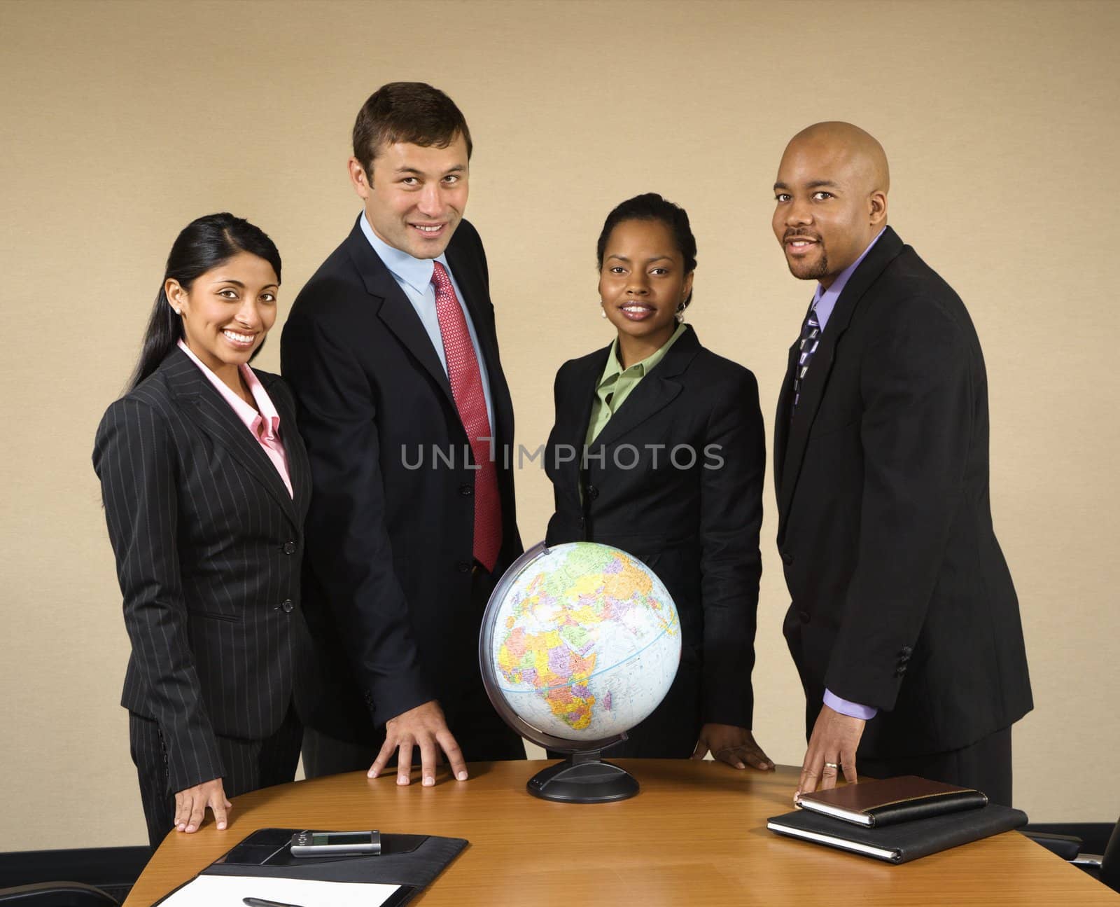 Corporate businesspeople standing around world globe smiling.