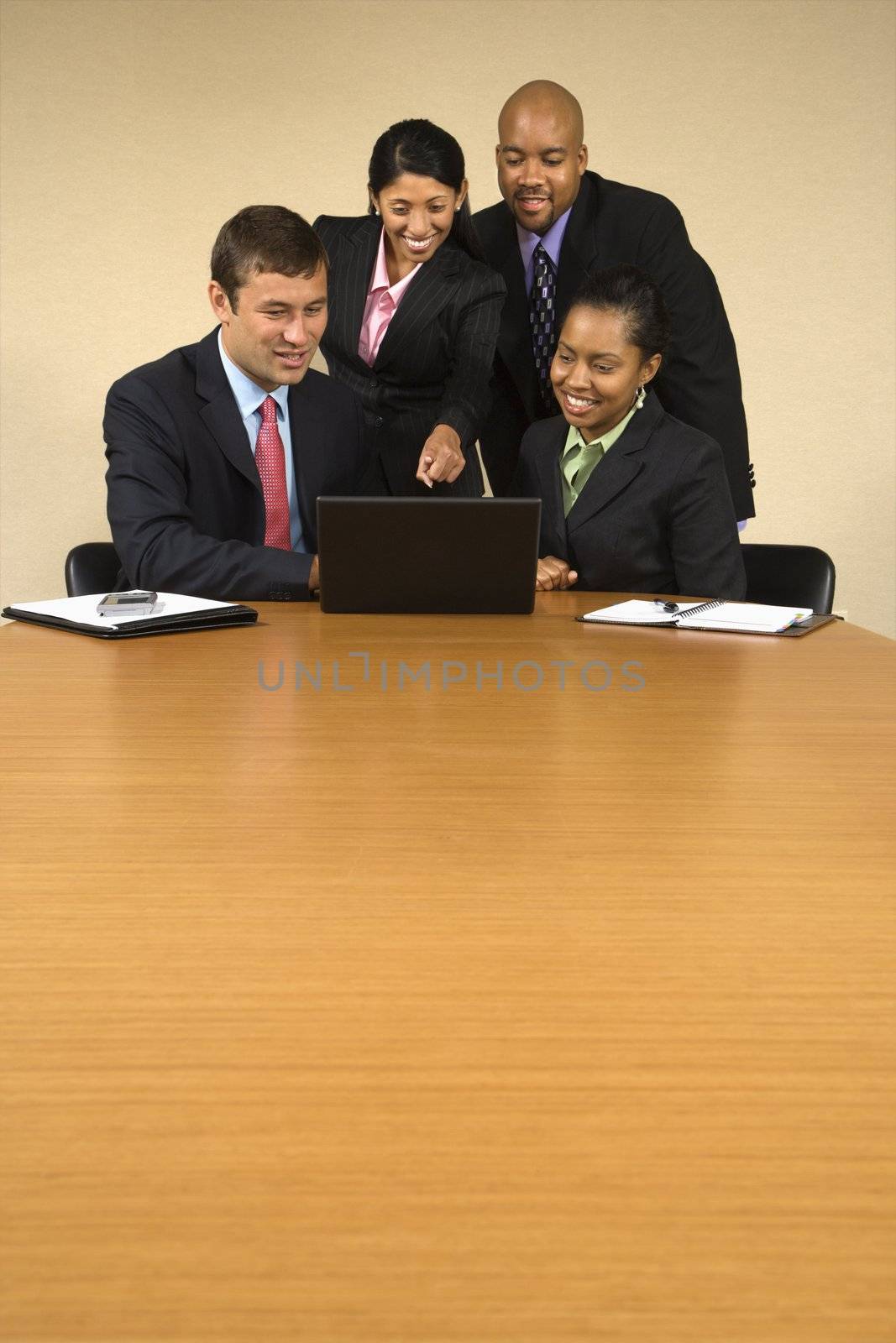 Businesspeople gathered around laptop computer looking at monitor and smiling.