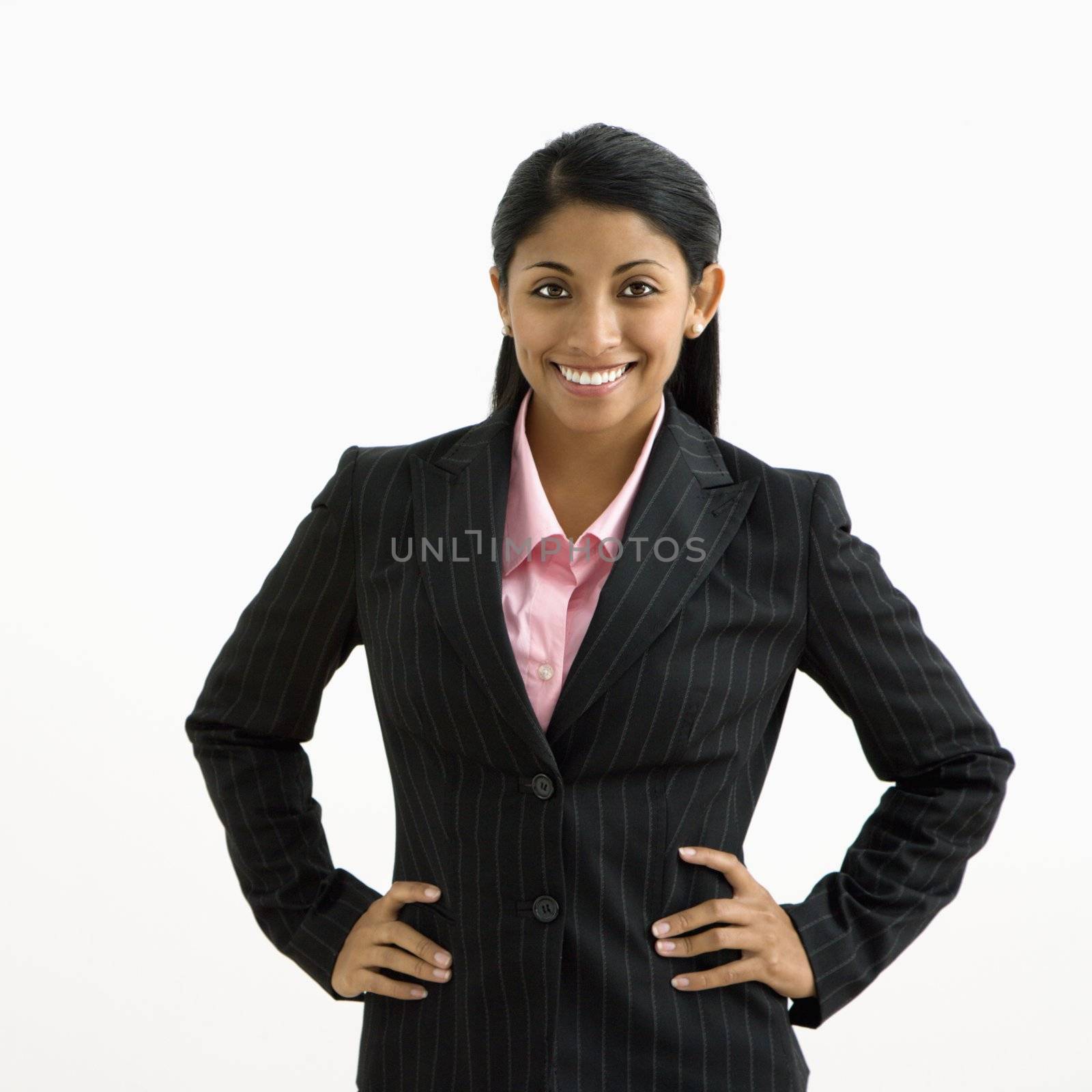 Portrait of smiling businesswoman with hands on hips against white background.