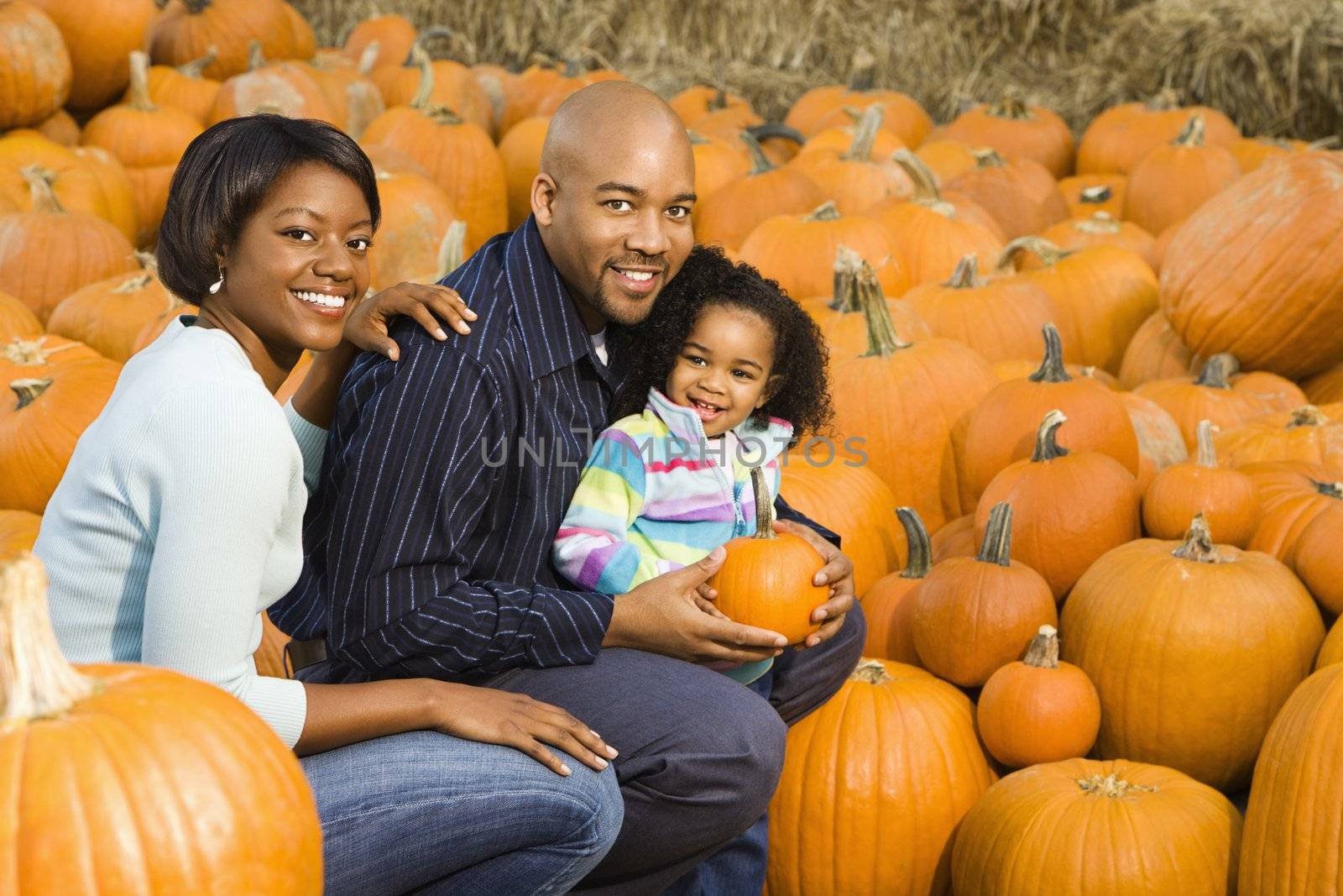 Parents and daughter picking out pumpkin and smiling at outdoor market.