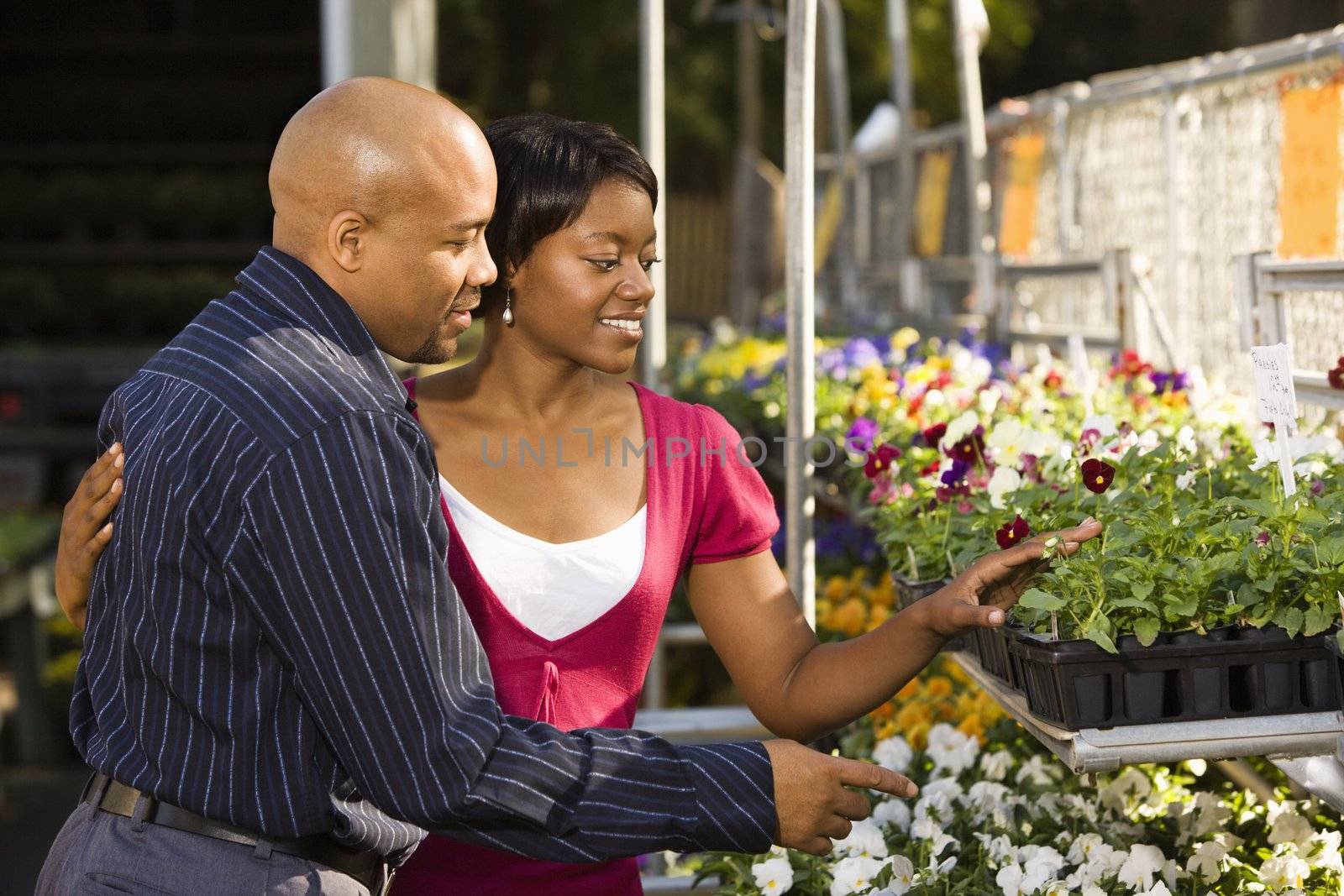Happy smiling couple picking out flowers at outdoor plant market.