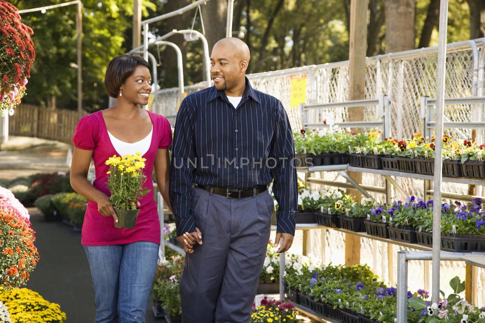 Happy smiling couple picking out flowers at outdoor plant market walking and holding hands.