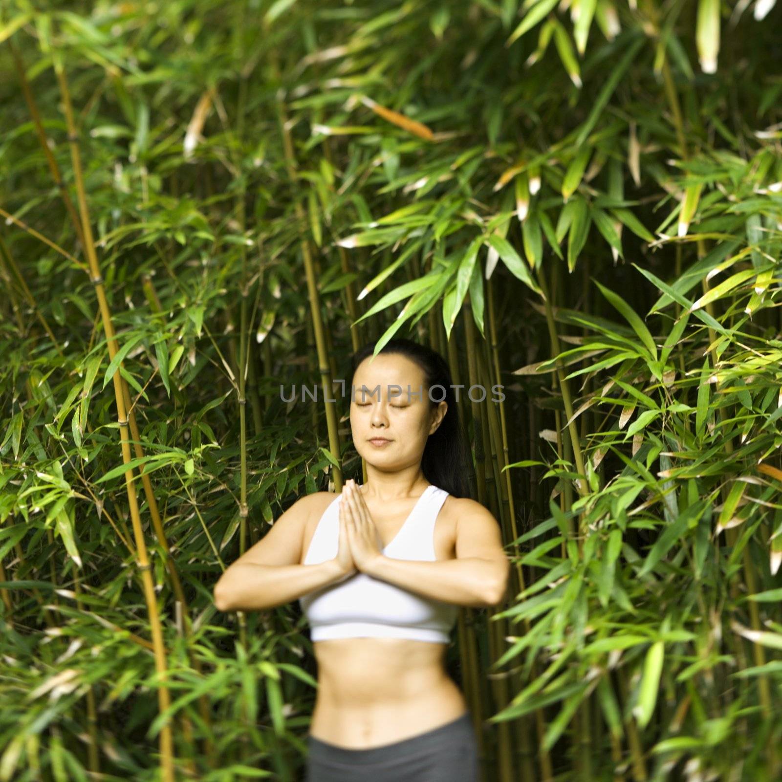 Half length portrait of Asian American woman in fitness attire standing in yoga position in bamboo forest in Maui, Hawaii.