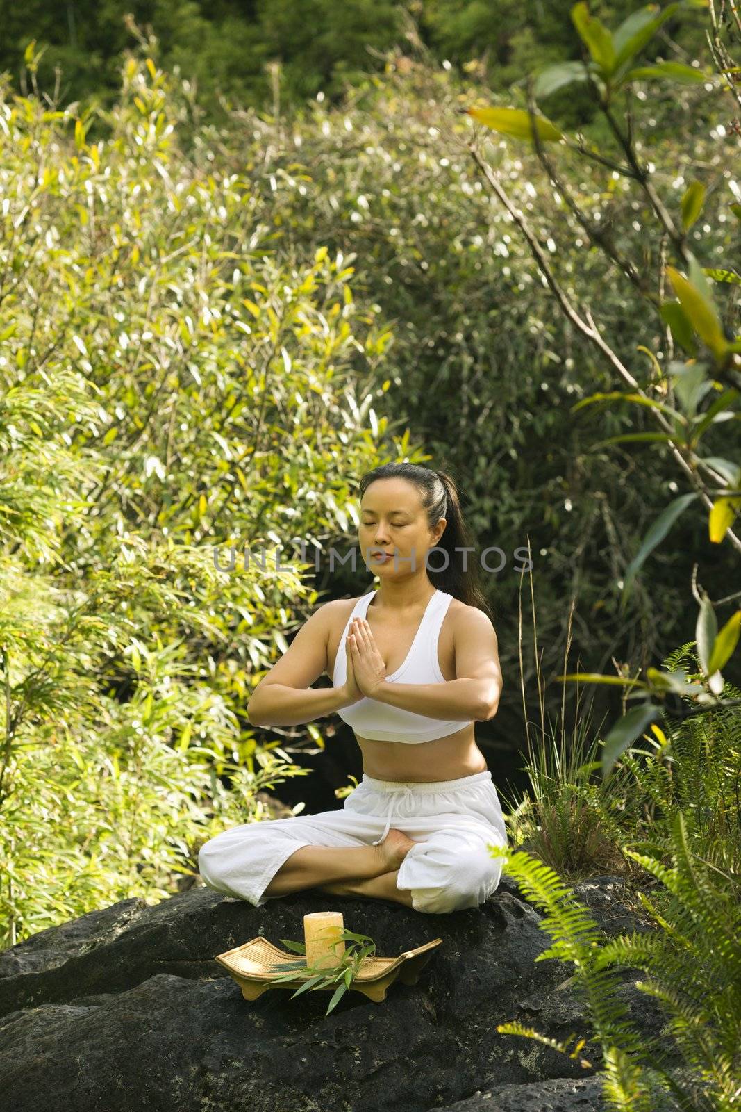 Asian American woman sitting on boulder in forest meditating with candle in Maui, Hawaii.