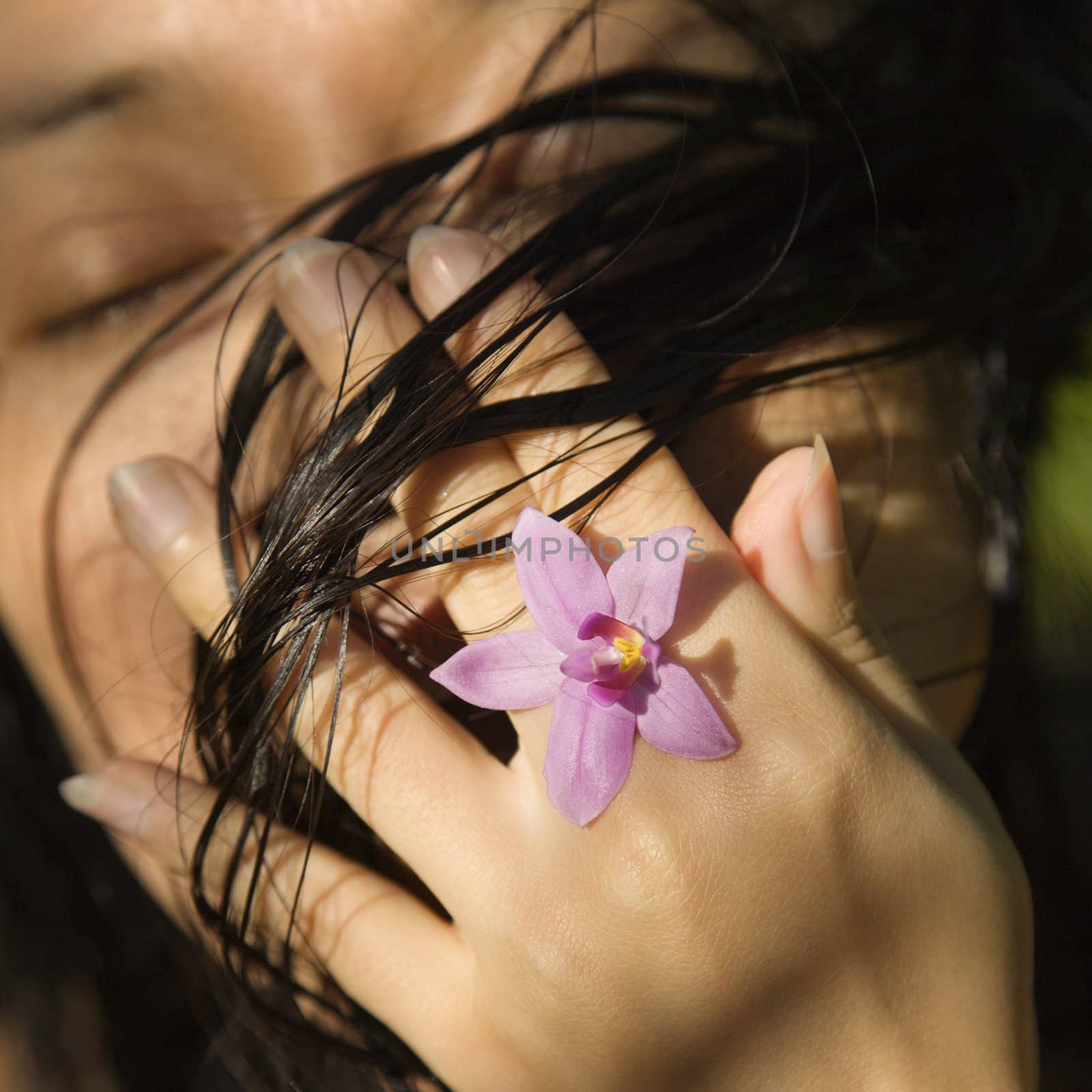 Mid-adult Asian female holding flower up to her face.