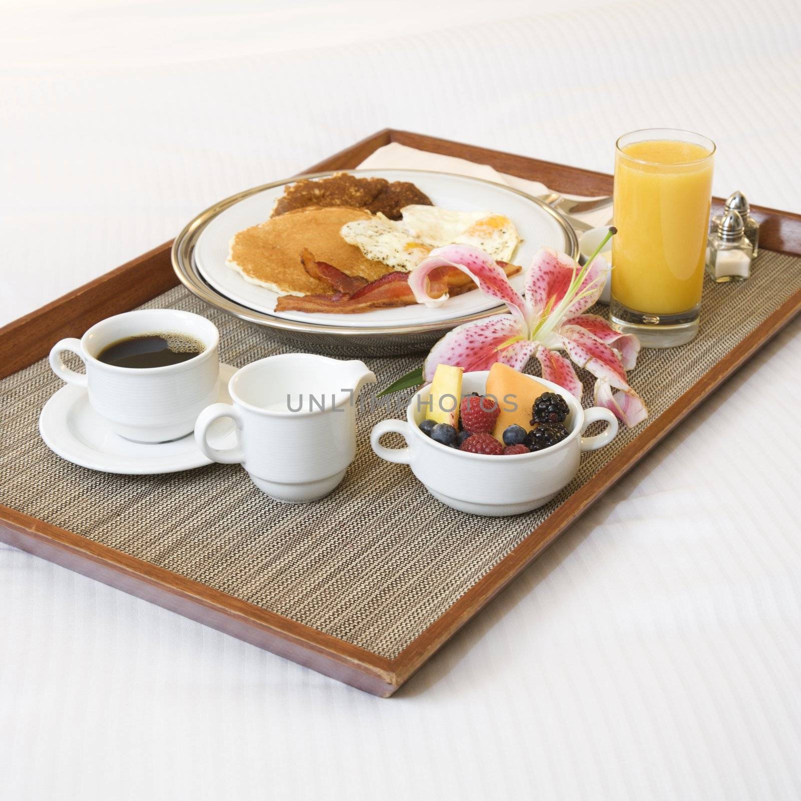 Close-up of breakfast tray laying on white bed.