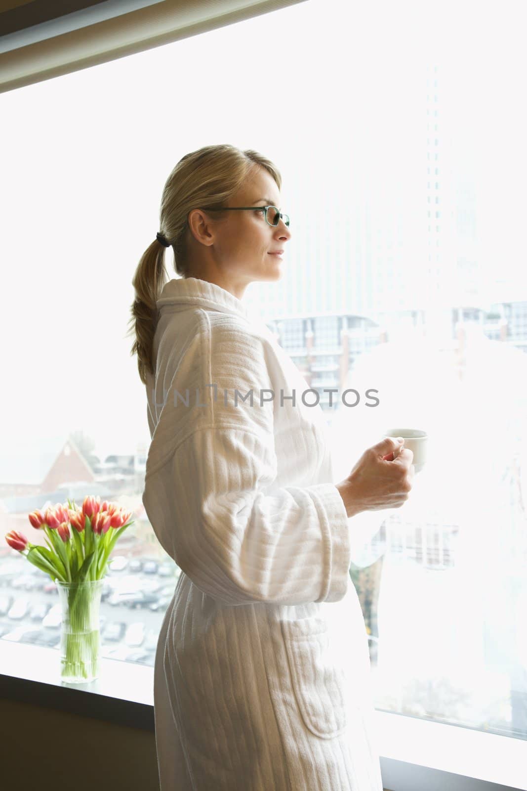 Mid-adult Caucasian woman with coffee cup looking out window.