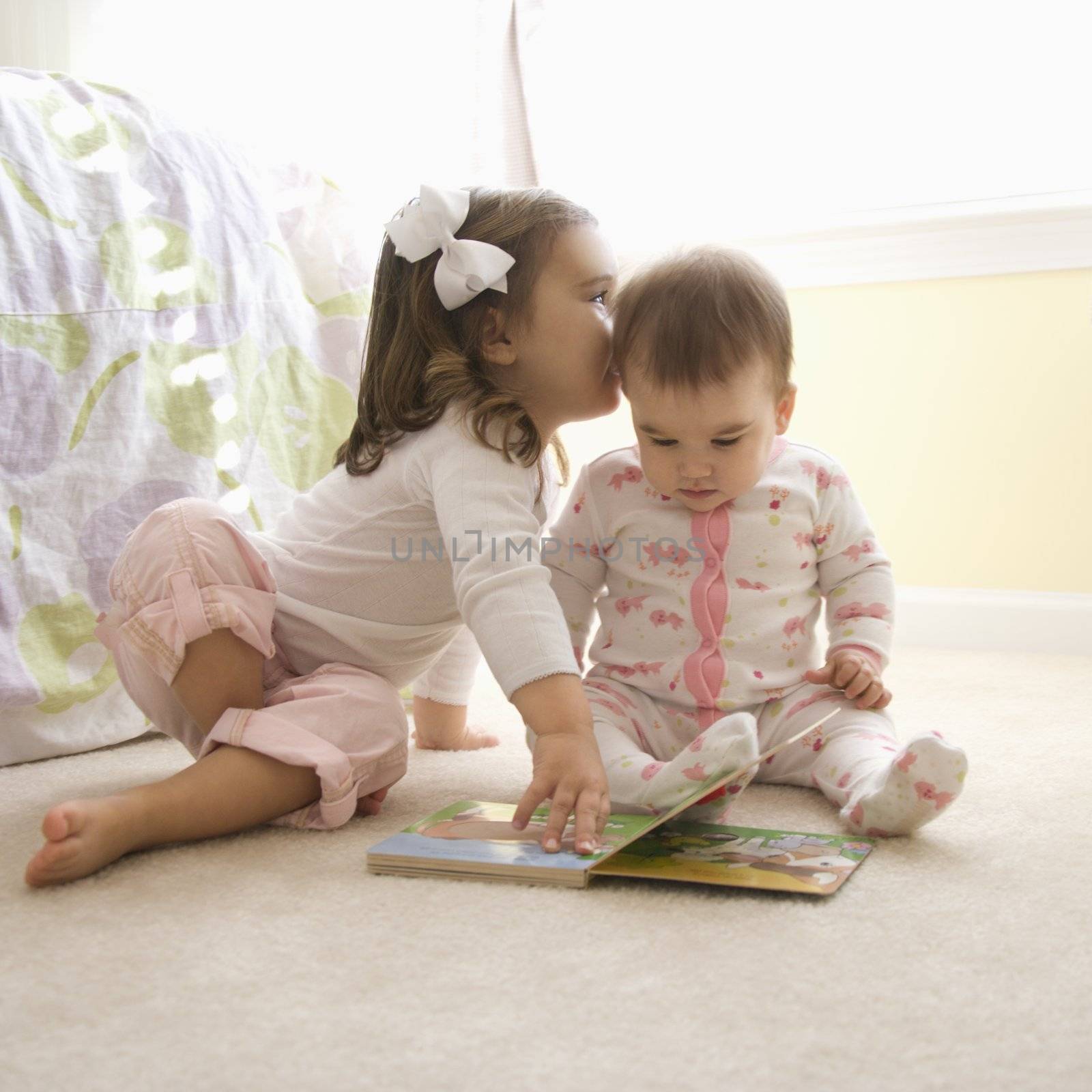 Caucasian girl children sitting on bedroom floor looking at book.
