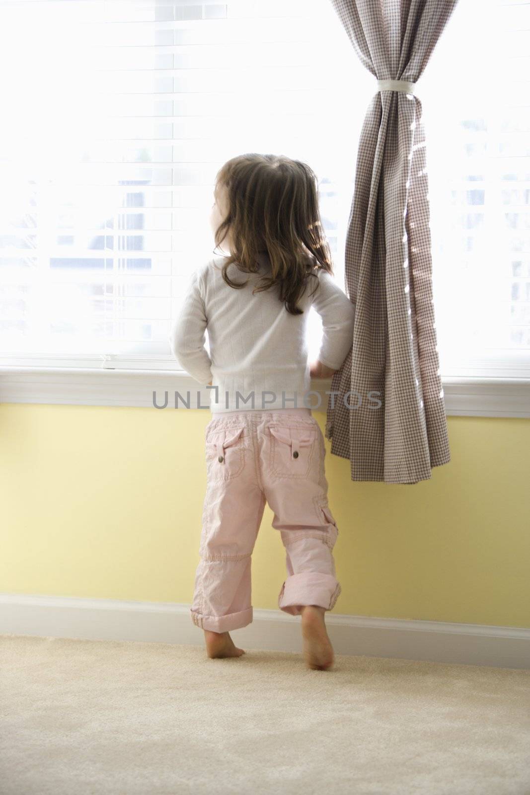 Caucasian girl toddler standing on tip toes looking out of window.