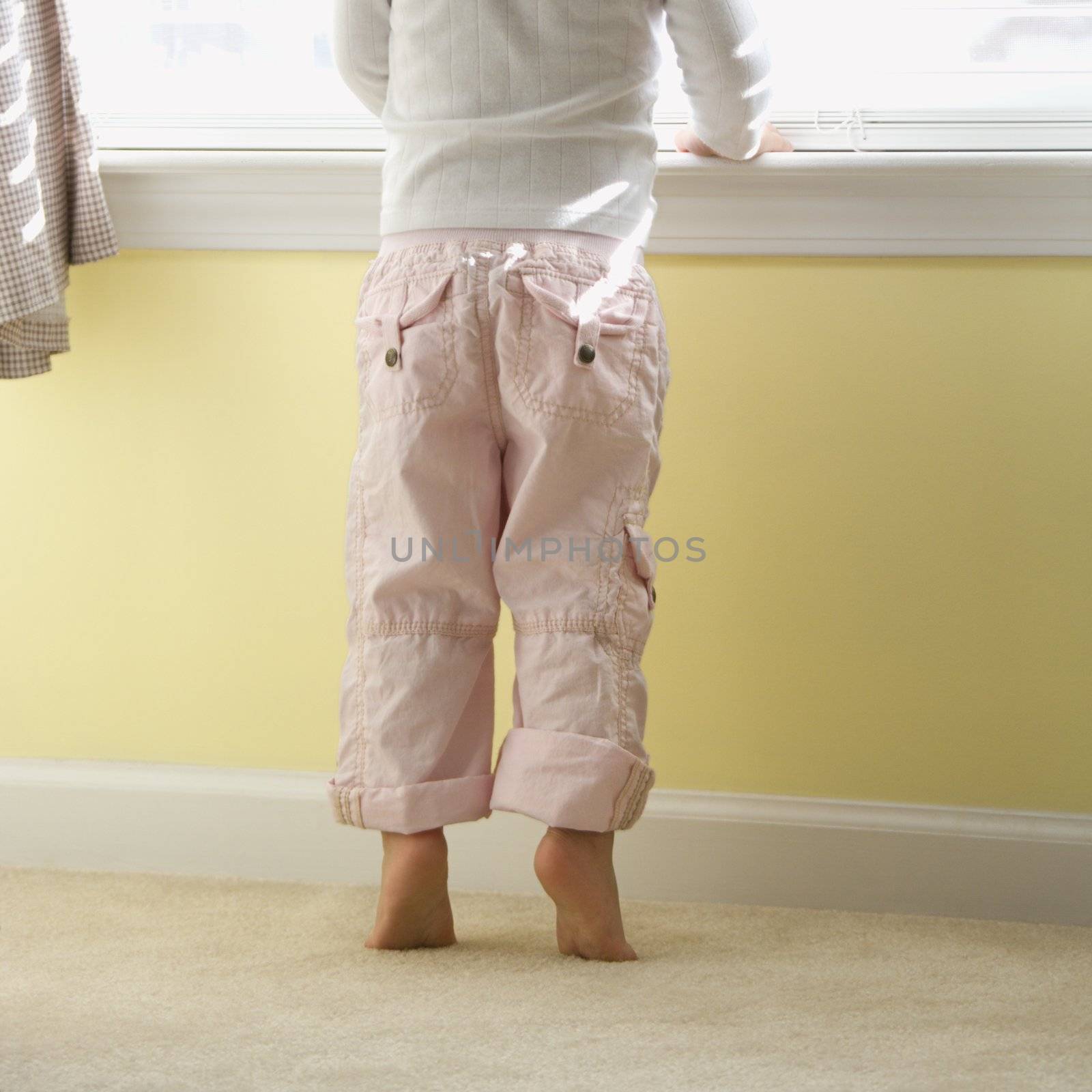 Caucasian girl toddler standing on tip toes looking out of window.