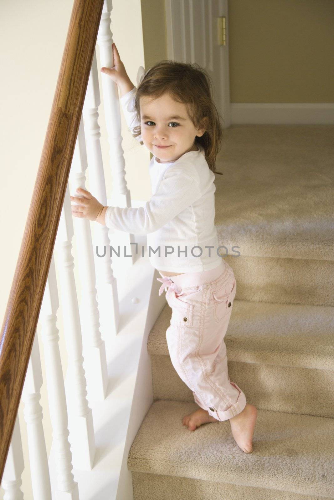 Caucasian girl toddler standing on carpeted stairs holding onto railing.