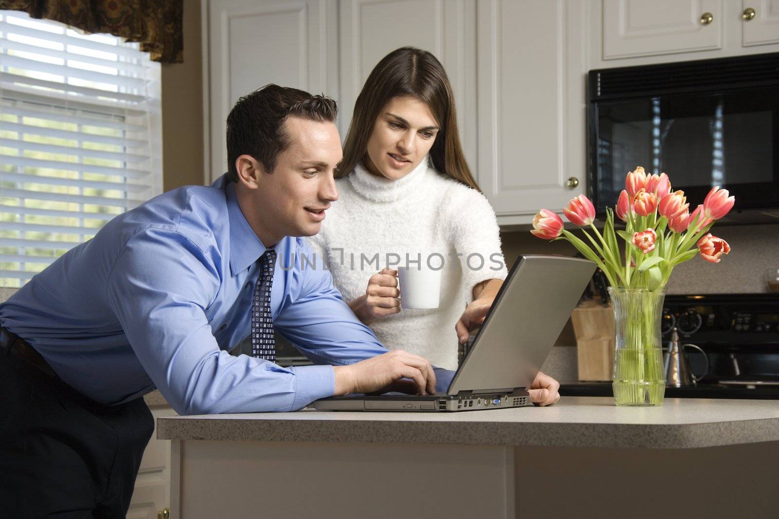 Caucasian couple in kitchen with coffee looking at laptop computer.