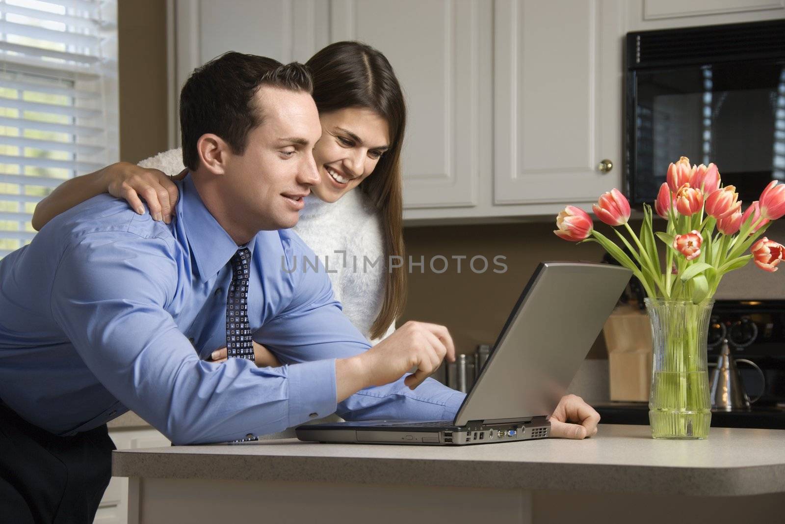Caucasian couple in kitchen looking at laptop computer.