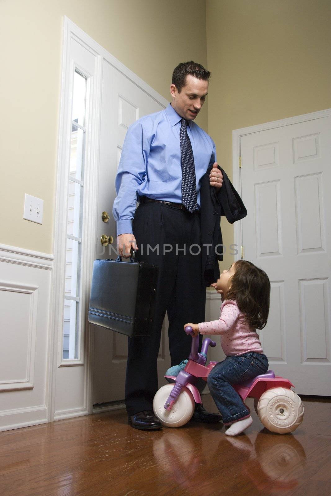 Caucasian businessman at door with briefcase with daughter looking up at him.