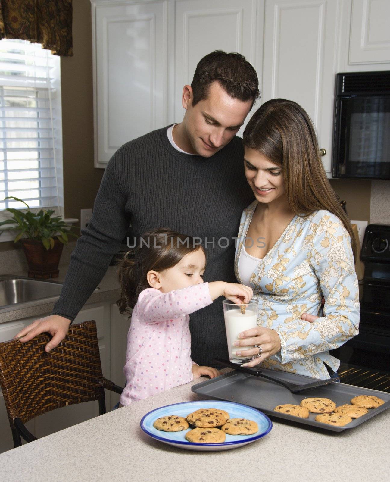 Caucasian mother and father with daughter eating cookies and milk.