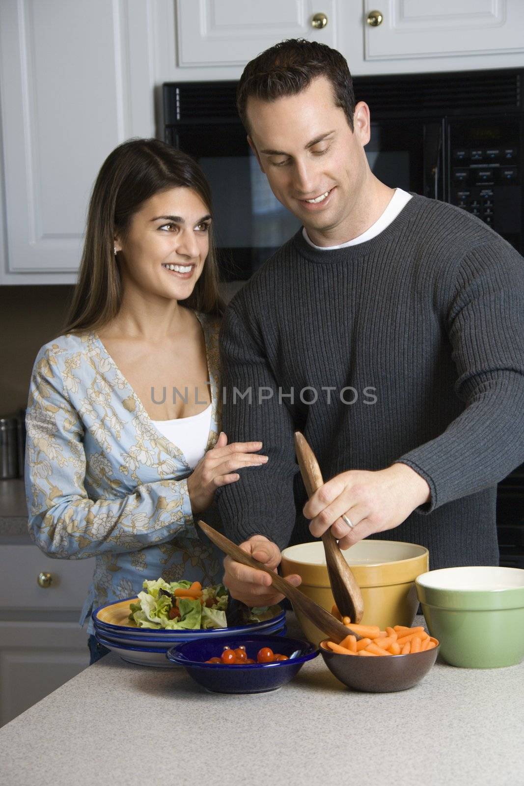 Caucasian couple making salad at kitchen counter.
