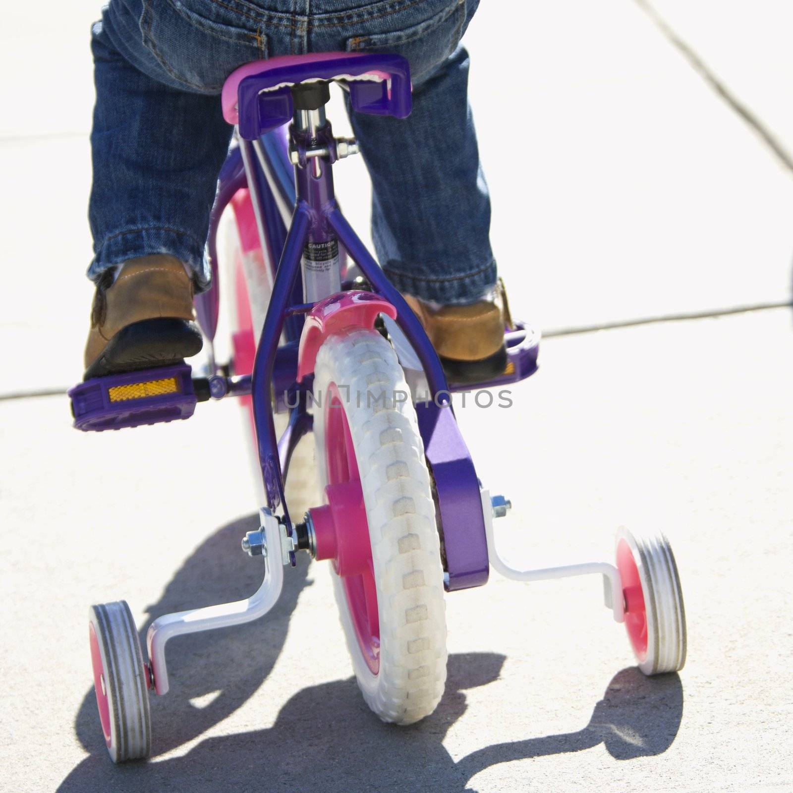 Back view of girl riding bicycle with training wheels.