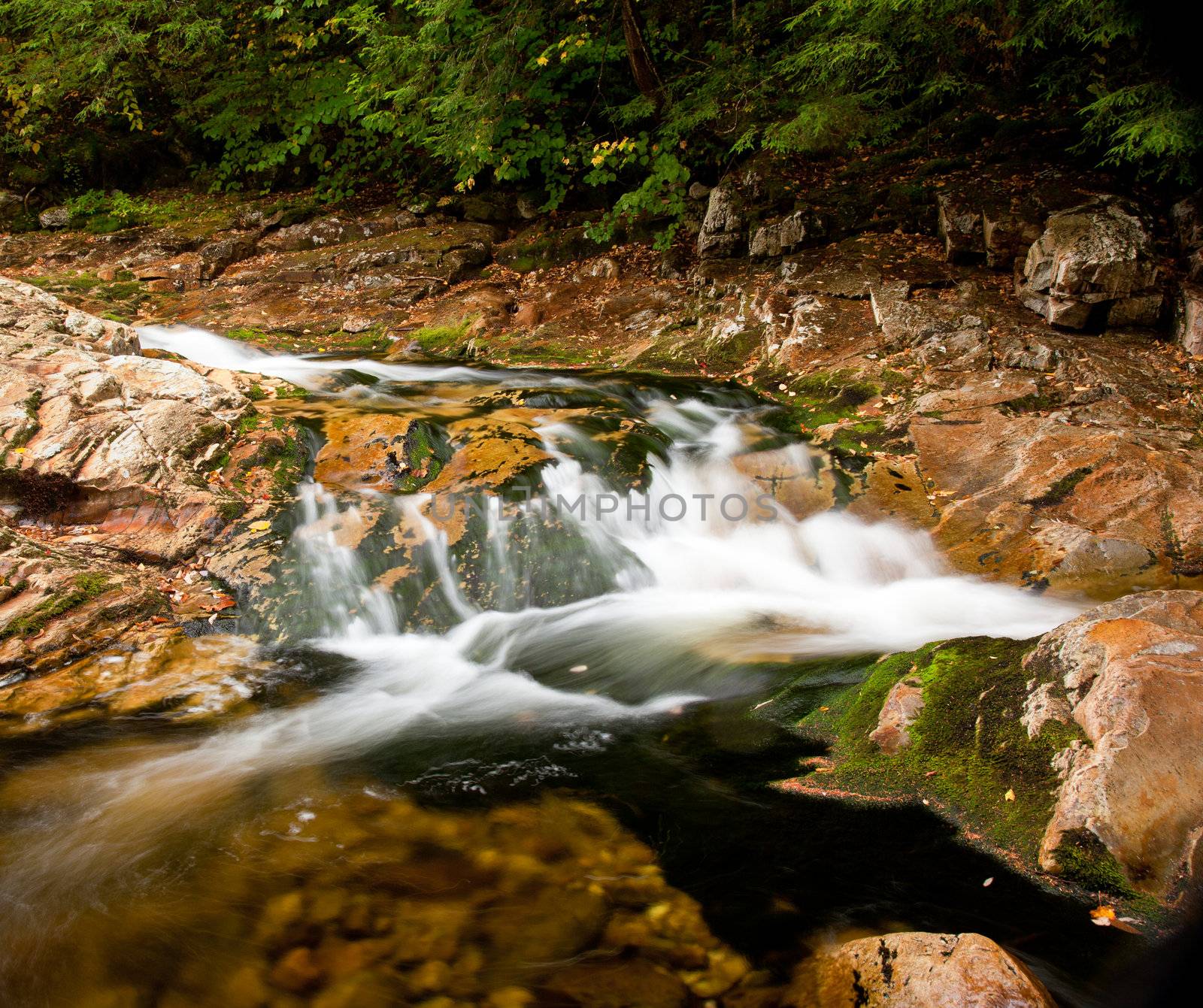 Long duration image of water flowing over boulders and mossy rocks in autumn