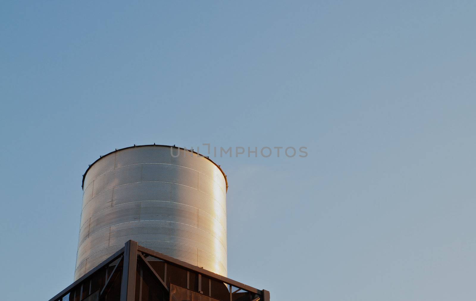 Brightly late sun lit steel water tank on tower against clear blue sky
