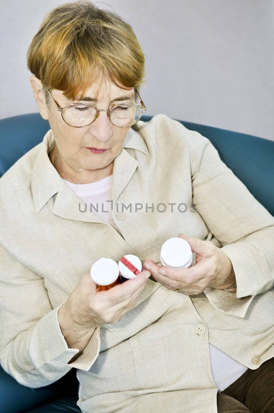 Elderly woman reading pill bottles by elenathewise